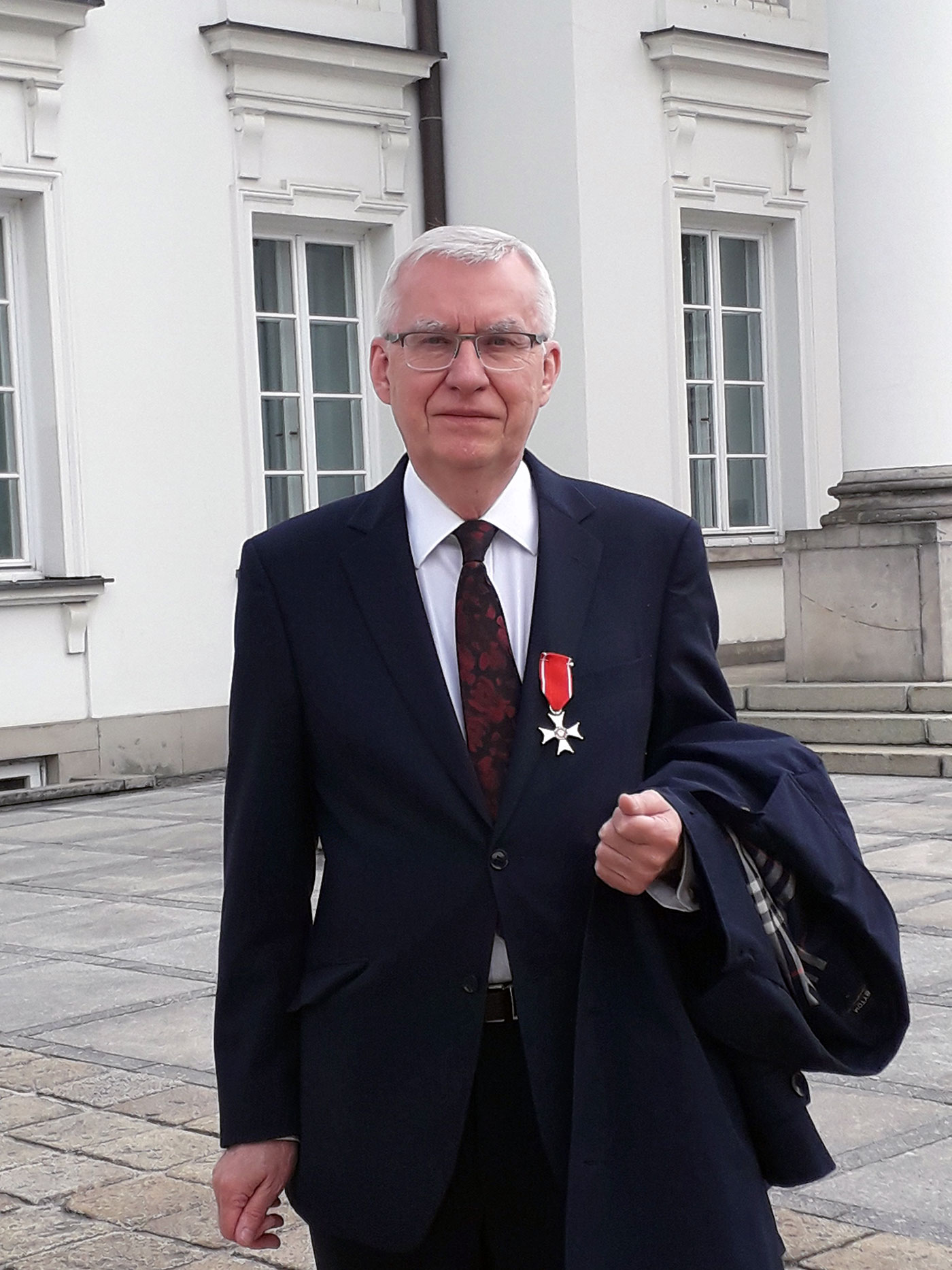 Poważny starszy mężczyzna w okularach w garniturze odznaczony krzyżem Kawalerskim Orderu Odrodzenia Polski