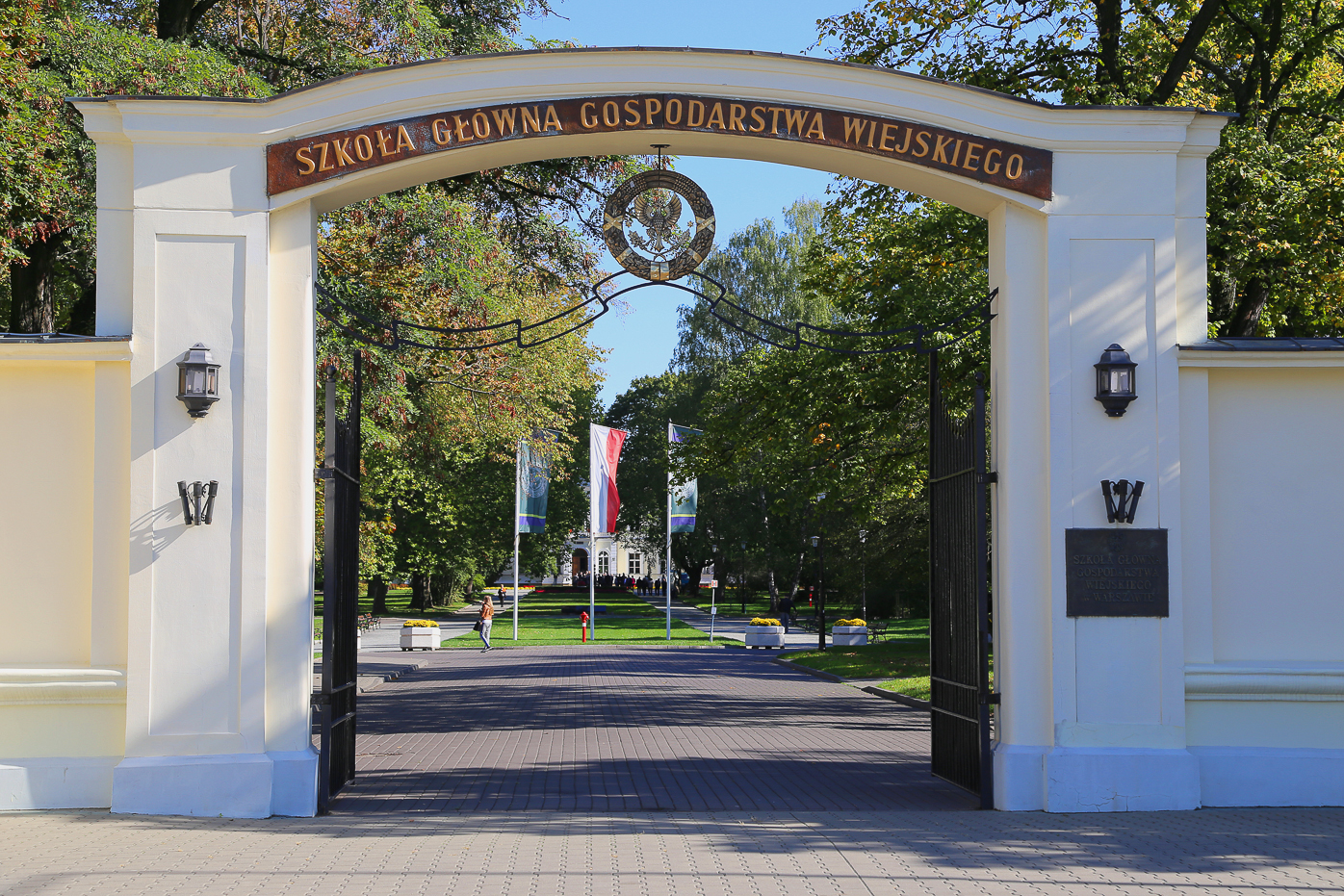 Główna brama Szkoły Głównej Gospodarstwa Wiejskiego w Warszawie, z widocznym napisem uczelni i aleją prowadzącą na kampus.