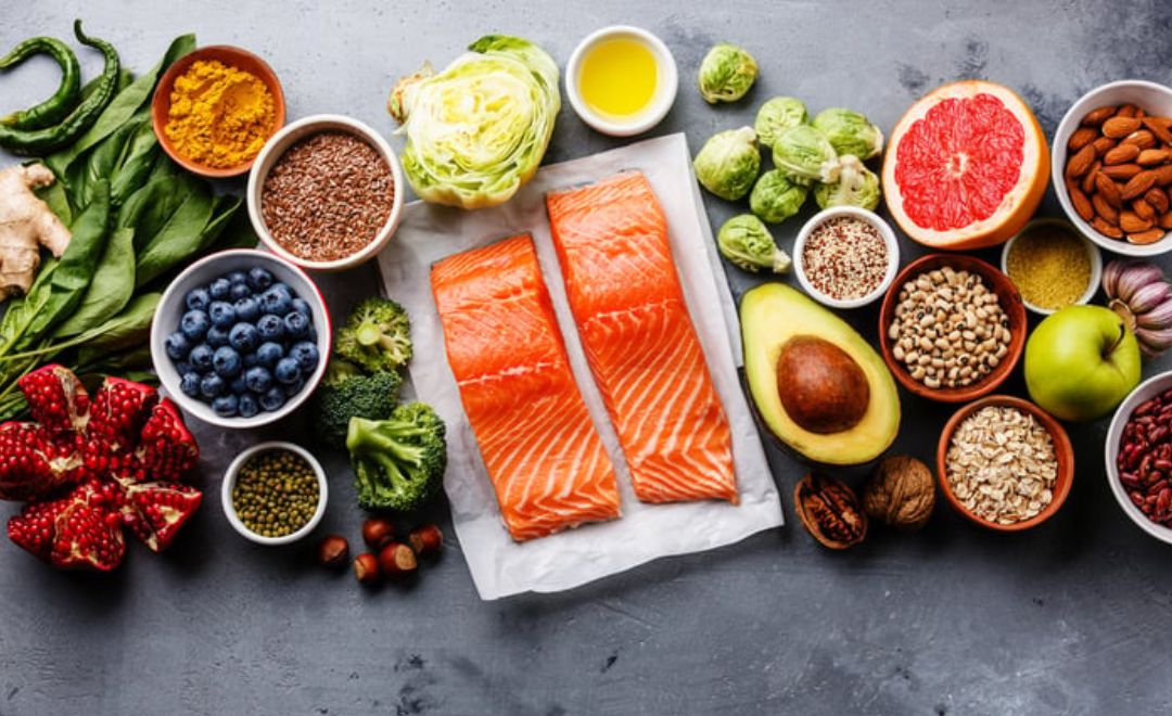 Kompozycja zdrowych produktów spożywczych: filety z łososia, warzywa, owoce, orzechy, nasiona, rośliny strączkowe i oliwa z oliwek.