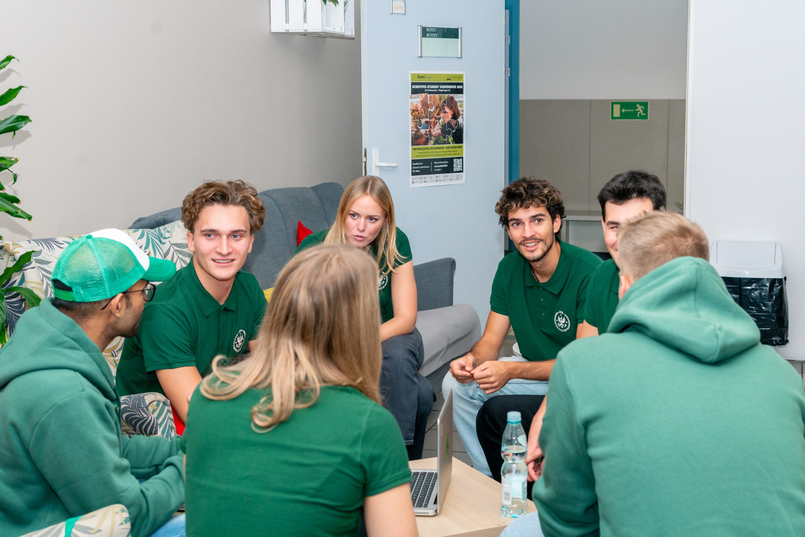 Grupa studentów siedzi w kręgu w przestrzeni wspólnej kampusu SGGW i rozmawia podczas spotkania. Na stoliku przed nimi znajduje się otwarty laptop.
